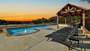 Una piscina con fuente, sillas de descanso y una pérgola de madera.