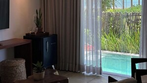 Un salon moderne doté d’un téléviseur à écran plat, d’une table en bois, d’un canapé, d’un meuble et offrant une vue sur une piscine et une végétation tropicale.