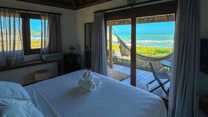 Une chambre avec un lit, une vue sur l’océan et un balcon équipé d’une table et de chaises.