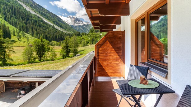 Un balcón con mesa y sillas, con vistas a un paisaje montañoso.