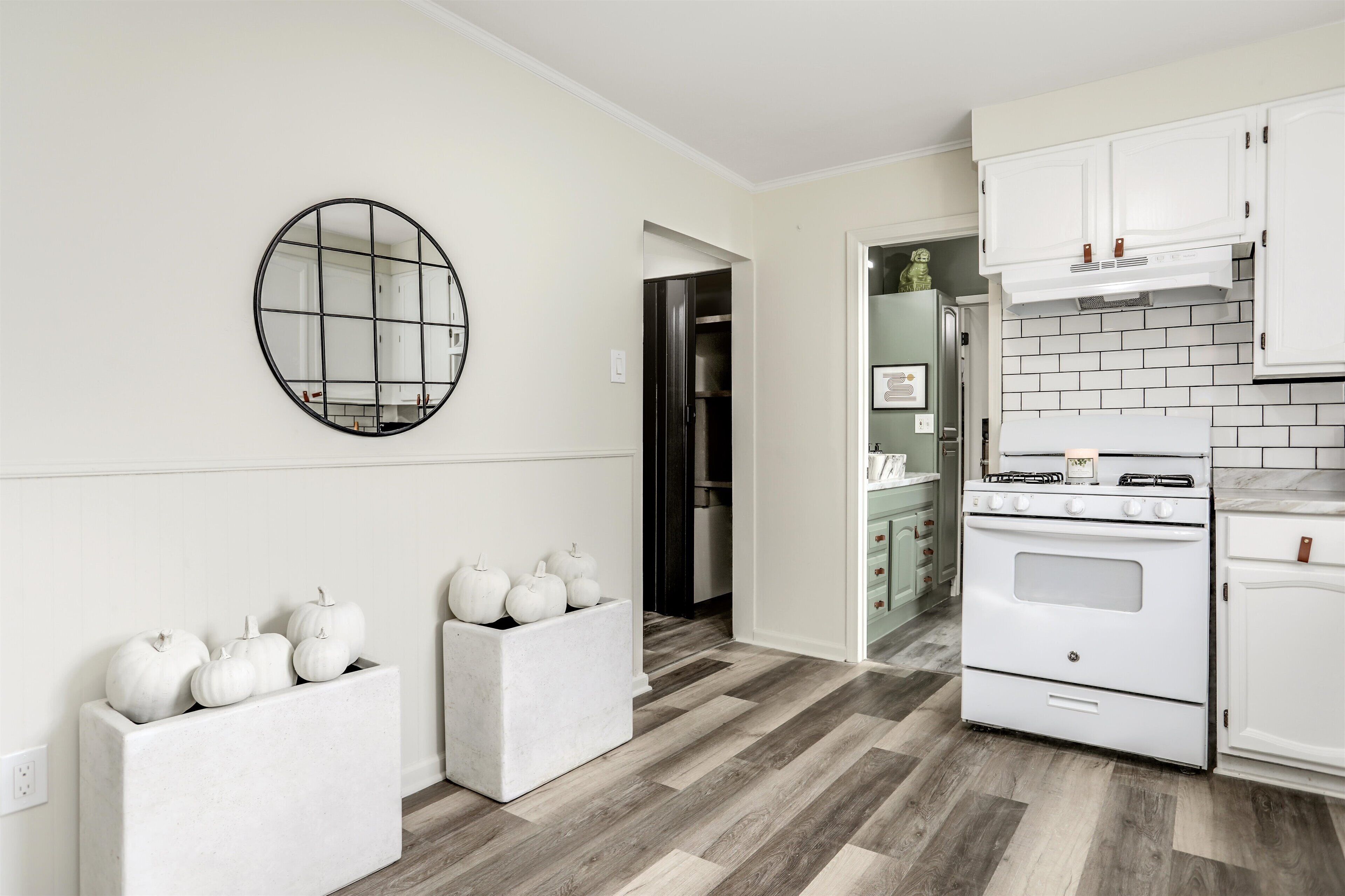 A modern kitchen with white cabinetry, a round mirror, and a wooden floor.