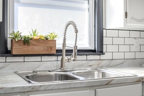 A kitchen with a double sink, a wooden planter with plants, and a window above the sink.