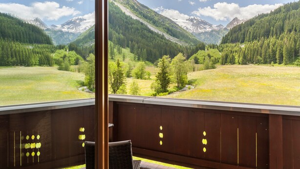 A balcony with a view of a mountainous landscape, wooden railing, and a chair.