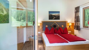 A bedroom with a wooden bed, red pillows, a mountain view, and a framed picture on the wall.
