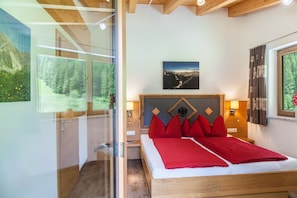 A bedroom with a wooden bed, red pillows, a mountain view, and a framed picture on the wall. - Apartment 'Haus Marchegg - Edelweiß' with Mountain View (Tux)