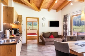A modern kitchen with a wooden ceiling, a dining area with a table and chairs, a sofa with a red cushion, and a TV mounted on the wall. - Apartment 'Haus Marchegg - Edelweiß' with Mountain View (Tux)