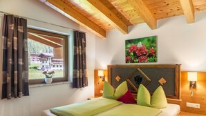 Een hotelkamer met een bed, een raam met gordijnen, uitzicht op gebouwen, een aan de muur hangend schilderij en een houten plafond.