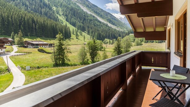 Een balkon met uitzicht op een bergachtig landschap, een houten terras en een tafel met stoelen.