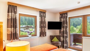 Een slaapkamer met een bed, een televisie, een stoel en grote ramen met uitzicht op een huis en bos.