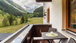 Een balkon met een tafel en stoelen, uitzicht op een bergachtig landschap, en een gebouw met een bord.