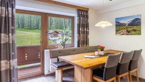 Een eetgedeelte met een houten tafel, bankjes en uitzicht op een bergachtig landschap door grote ramen.