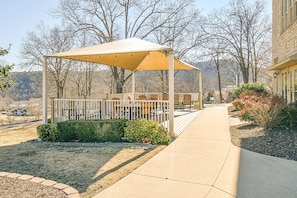 Relax in a serene outdoor space with a shaded bench and table, surrounded by a beautiful garden.