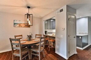 A dining area with a wooden table and chairs, a pendant light, and a painting on the wall.