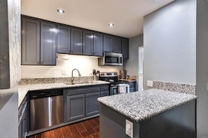 A modern kitchen with grey cabinets, a stainless steel dishwasher, a microwave, and a granite countertop.