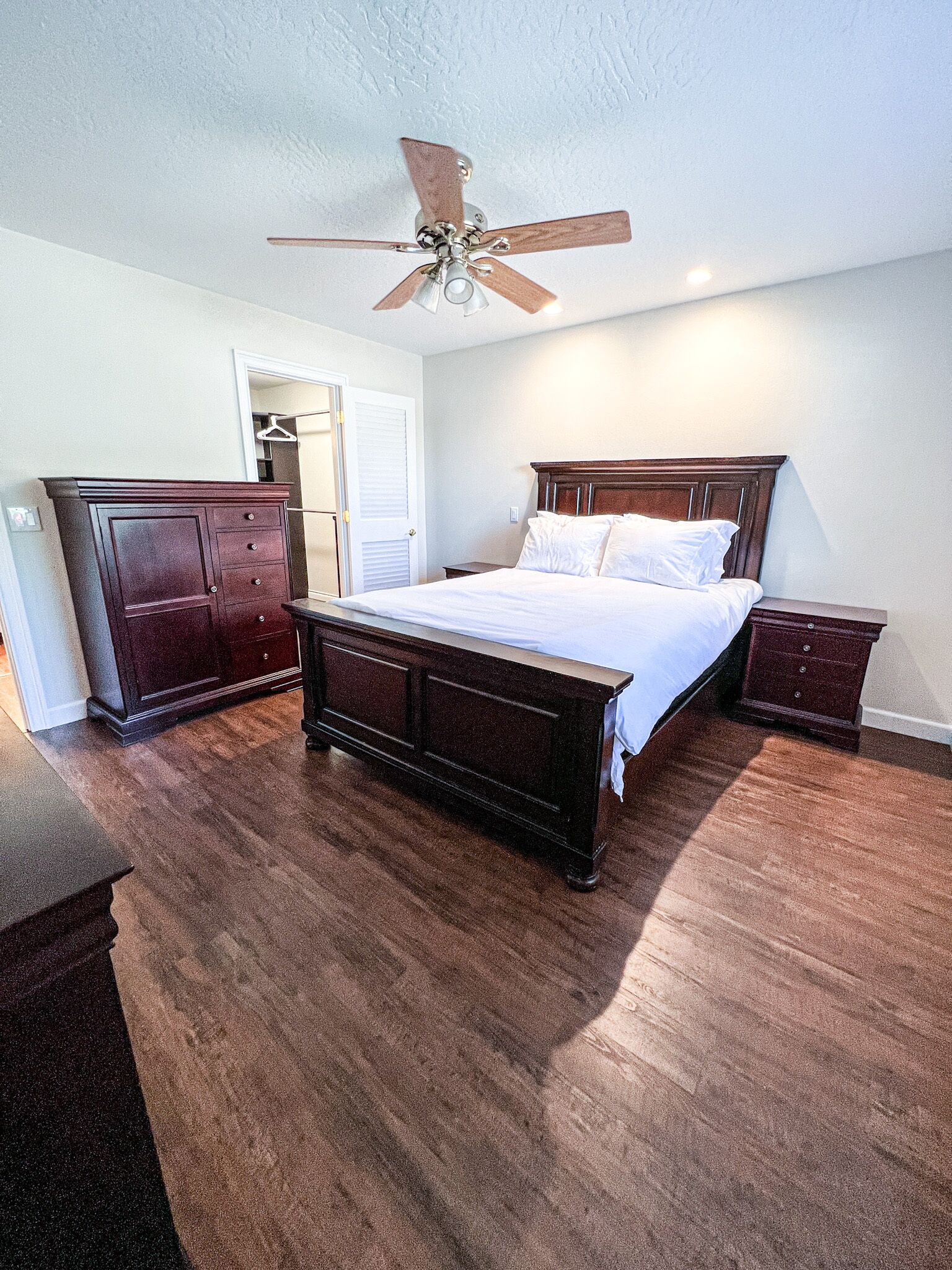 A bedroom with a wooden bed, a nightstand, a dresser, and a ceiling fan.