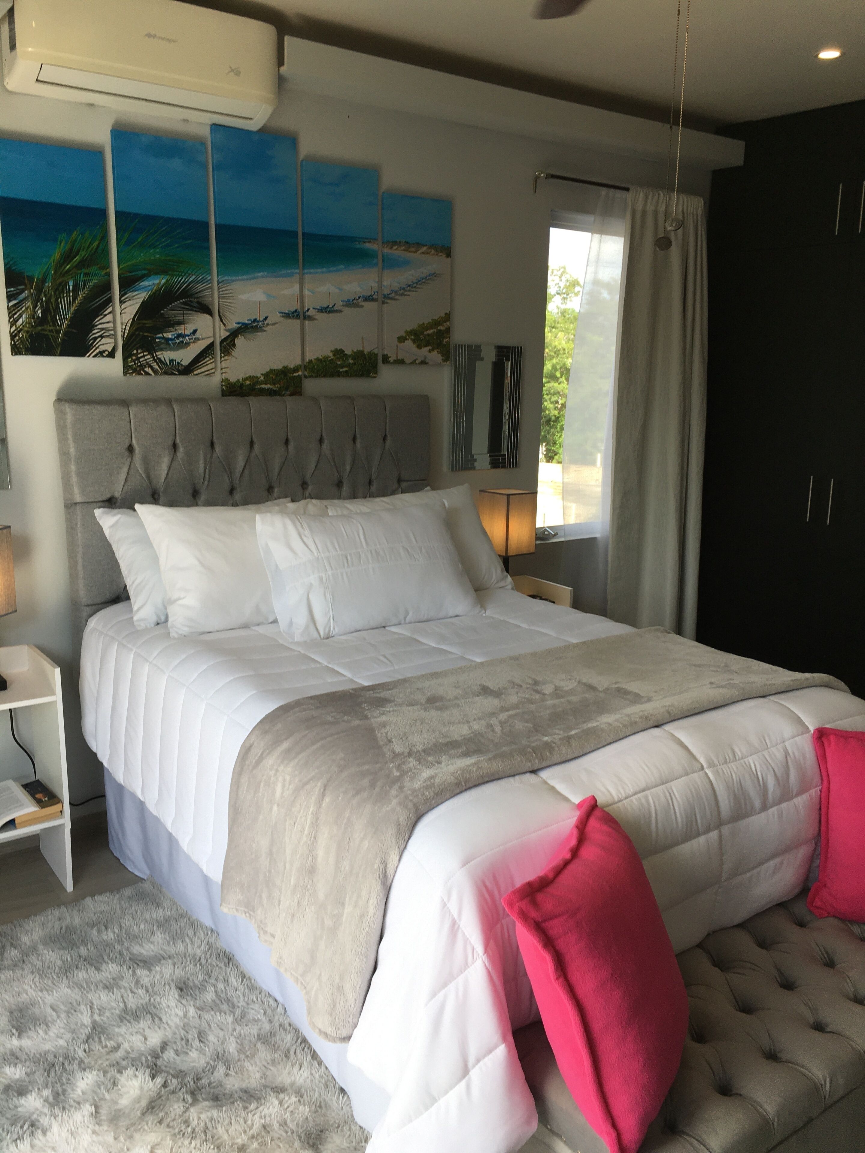 A bedroom with a large bed, a headboard, a nightstand, a lamp, and a window with curtains.