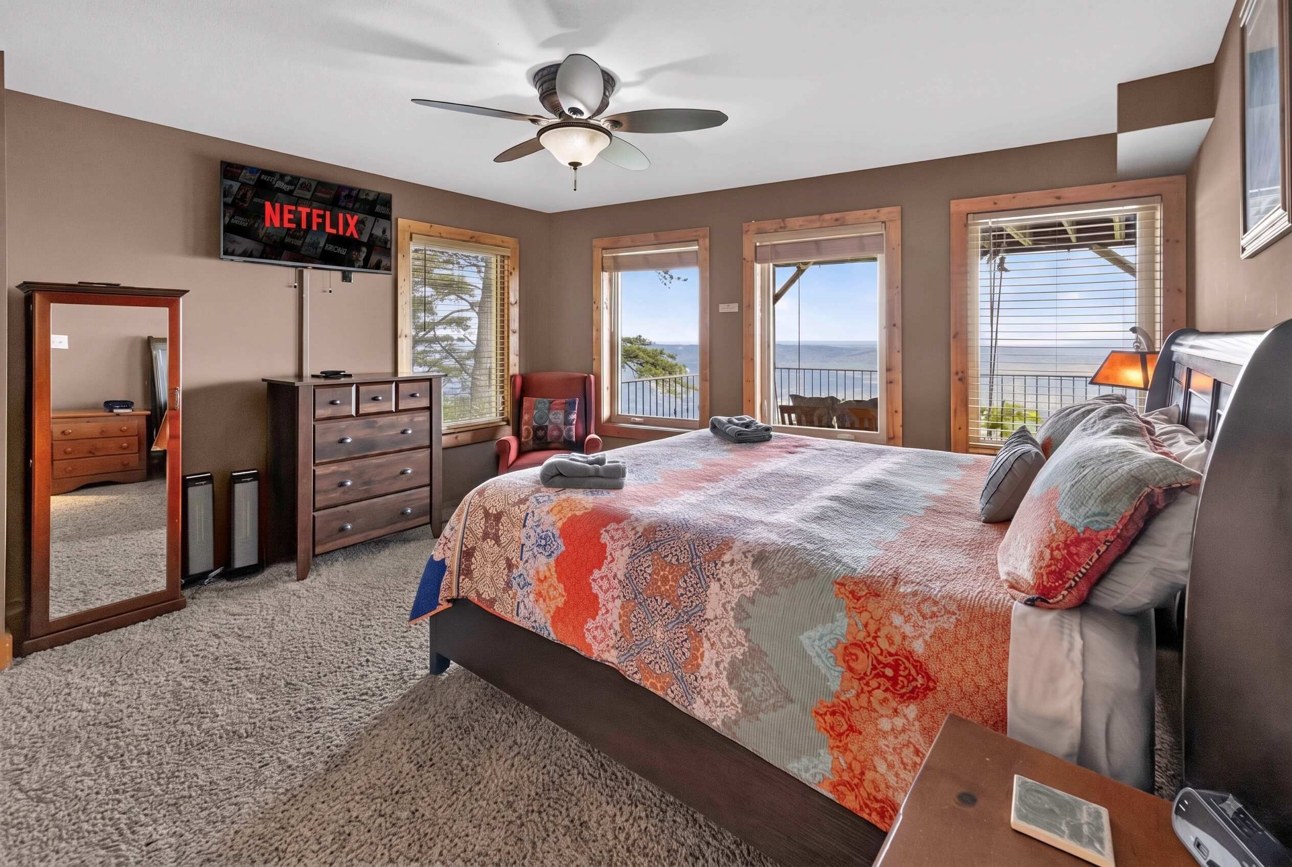 Quarto com cama, cômoda, televisão e vista para o exterior.
