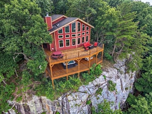 A wooden cabin with a balcony, surrounded by dense forest.