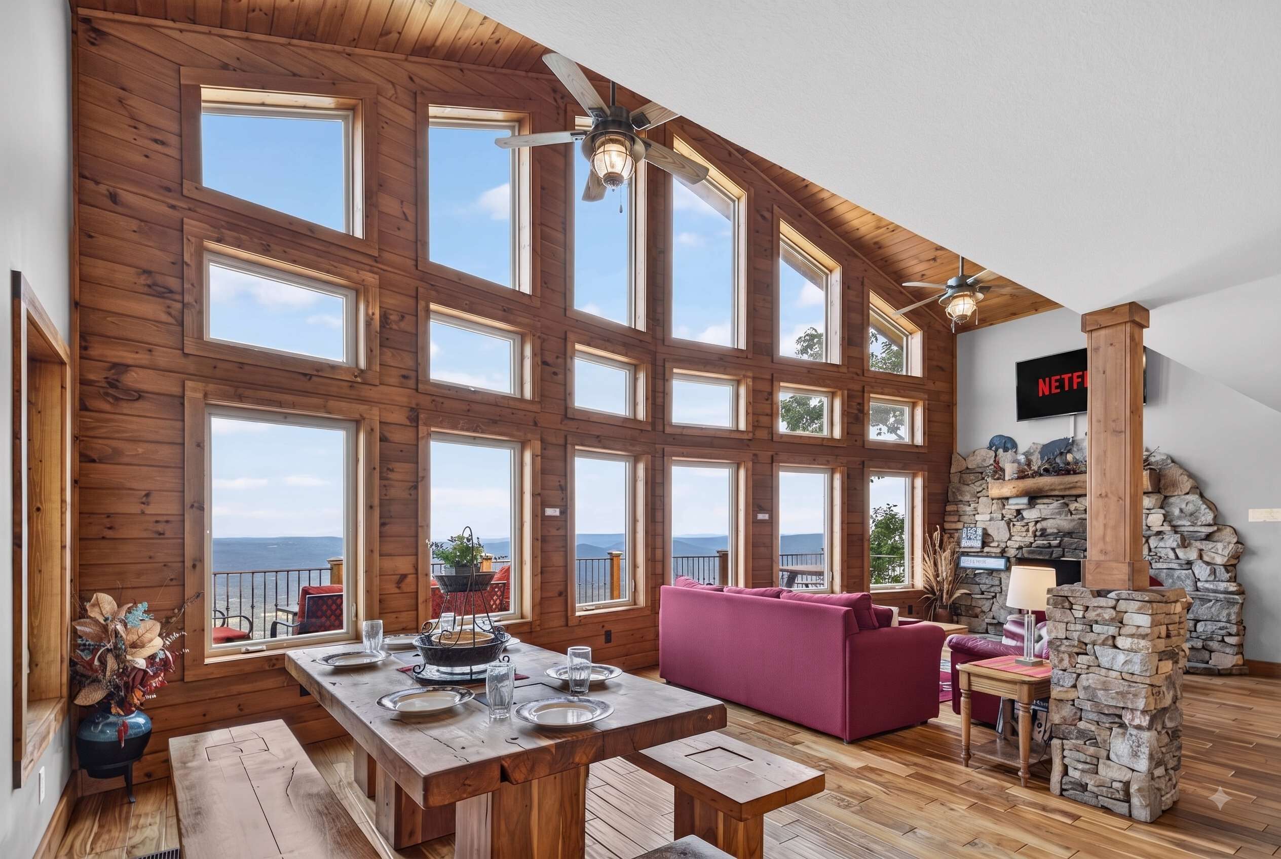 A spacious room with a high ceiling, large windows, a stone fireplace, and a cozy seating area.