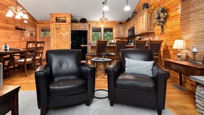 A cozy cabin-style interior with wooden walls, a dining area with a table and chairs, a kitchen with wooden cabinets, and two leather armchairs. - Welcome to our stunning 3-bedroom, 2-bathroom house nestled in the heart of Wintergreen, Virginia. (Wintergreen Resort)