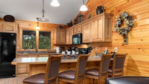 A wooden cabin kitchen with a central island, bar stools, and a large window. - Welcome to our stunning 3-bedroom, 2-bathroom house nestled in the heart of Wintergreen, Virginia. (Wintergreen Resort)