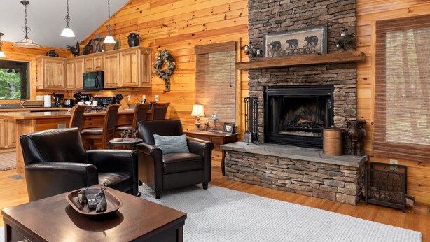 A cozy cabin interior with a stone fireplace, wooden walls, a dining area, and a kitchen with wooden cabinets and a microwave. - Welcome to our stunning 3-bedroom, 2-bathroom house nestled in the heart of Wintergreen, Virginia. (Wintergreen Resort)