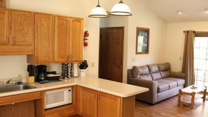 A kitchen with wooden cabinets, a microwave, and a coffee maker. There is a brown leather sofa and a small wooden table in the living area. - Stones Throw from Giant City Park, Wineries, Hiking, Biking, Hunting and more. (Makanda)