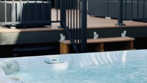 A hot tub with a control panel, a wooden deck, outdoor furniture, and a brick building in the background. - $0 Fees-Hot Tub, Lake View Oasis-Near Shops/Dining (Arvada)