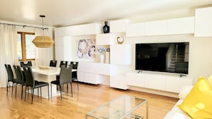 A modern living room with a dining area, white cabinetry, a flat-screen TV, and a glass coffee table. - Lake View Oasis with Hot Tub; Near Shops, dining, gas! Across from Park w/Lake  (Arvada)