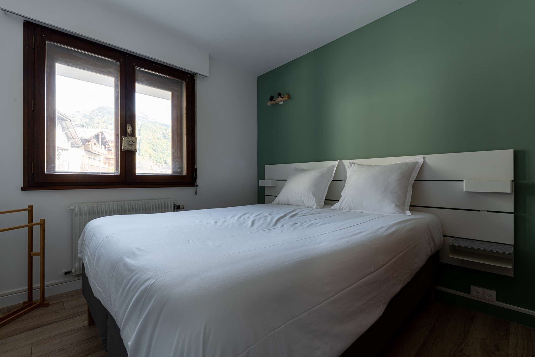 Un dormitorio con cama, ventana, radiador y estante con objetos.
