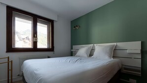 Un dormitorio con cama, ventana, radiador y estante con objetos.