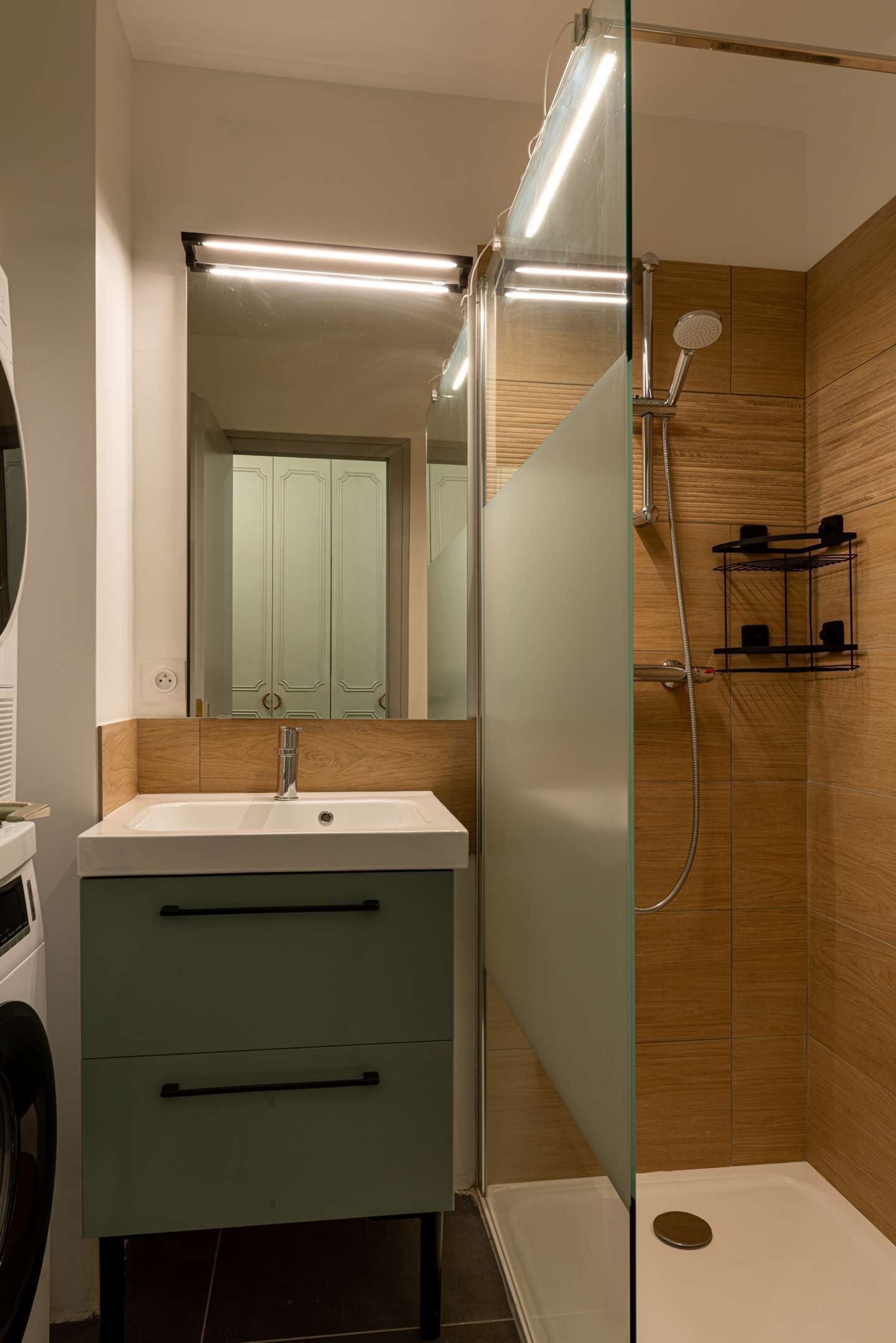 A modern bathroom with a glass shower enclosure, a sink with a mirror, and wooden paneling on the walls.