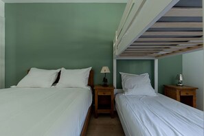 Et værelse med to enkeltsenge, hver med hvide sengetøj og en træsenggavl. To sengeborde, hver med en lampe og en lille dekorativ genstand. Væggene er malet grønne, og der er en køjeseng over sengene.
