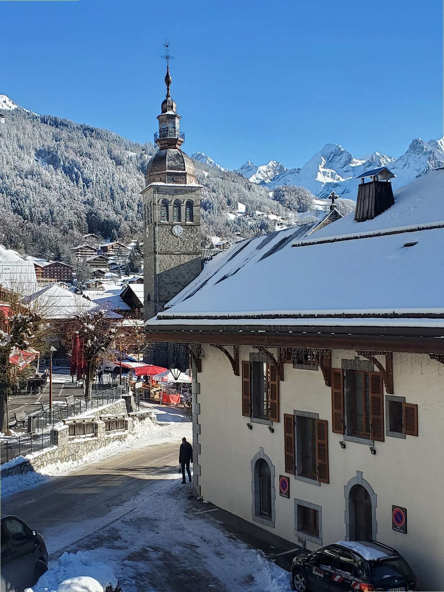 Ein schneebedecktes Dorf mit traditioneller Architektur, darunter ein Kirchturm und ein Gebäude mit Holzhinterfenstern.