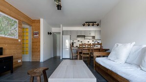 Una sala de estar moderna con piso de madera, un sofá blanco, una mesa de centro de madera y un televisor sobre un mueble de madera.