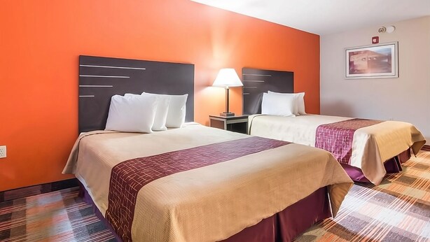 Habitación de hotel con dos camas, una mesita de noche, una lámpara y un cuadro en la pared.