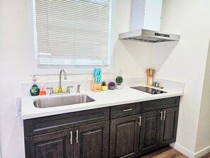A kitchen with a double sink, dark cabinets, a window with blinds, and a stainless steel range hood.