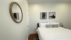 A bedroom with a bed, a round mirror, two abstract paintings, and a nightstand with a lamp.