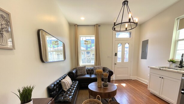 A modern living room with a black leather sofa, a coffee table, and wicker baskets. There is a kitchen area with a sink and cabinets.