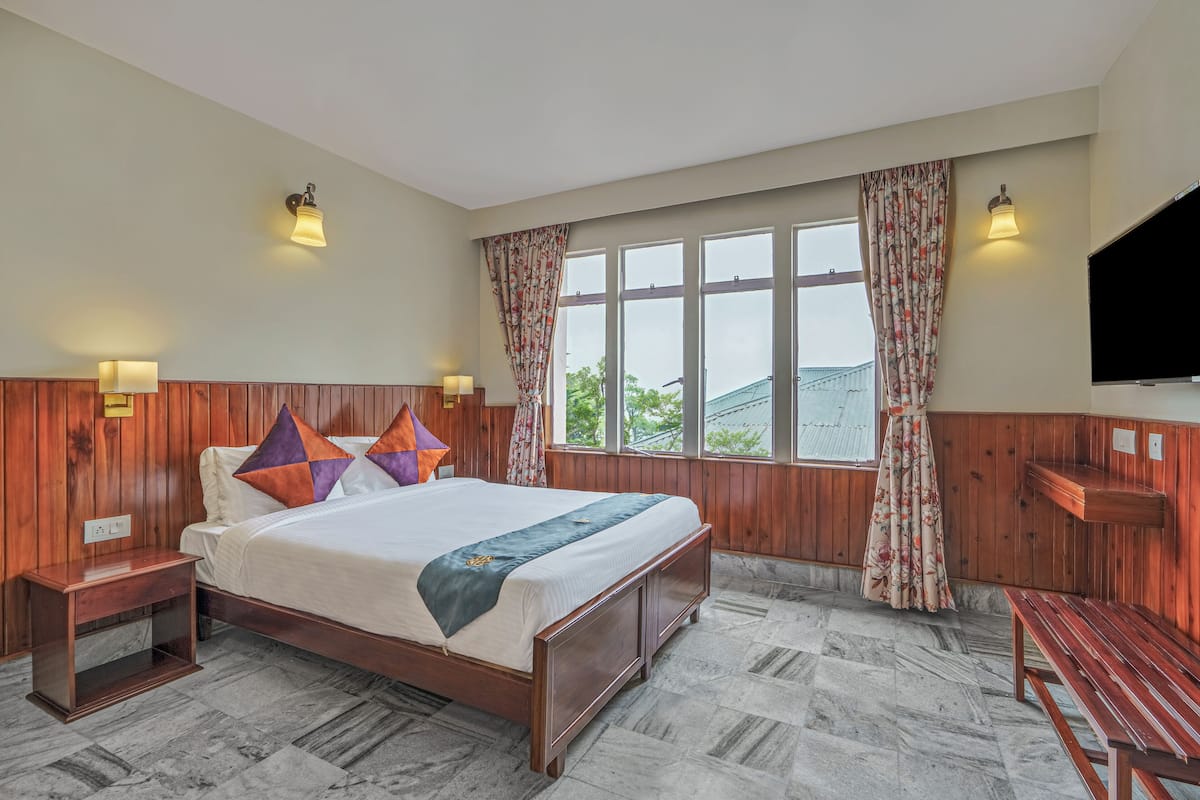 A hotel room with a wooden bed, a bench, a TV, and a window with curtains.