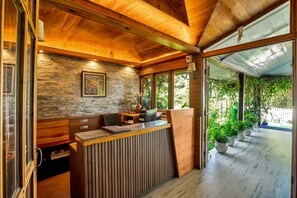 A reception area with a stone wall, wooden ceiling, and a view of a garden through large windows. - Sterling Park Kalimpong (Kalimpong)