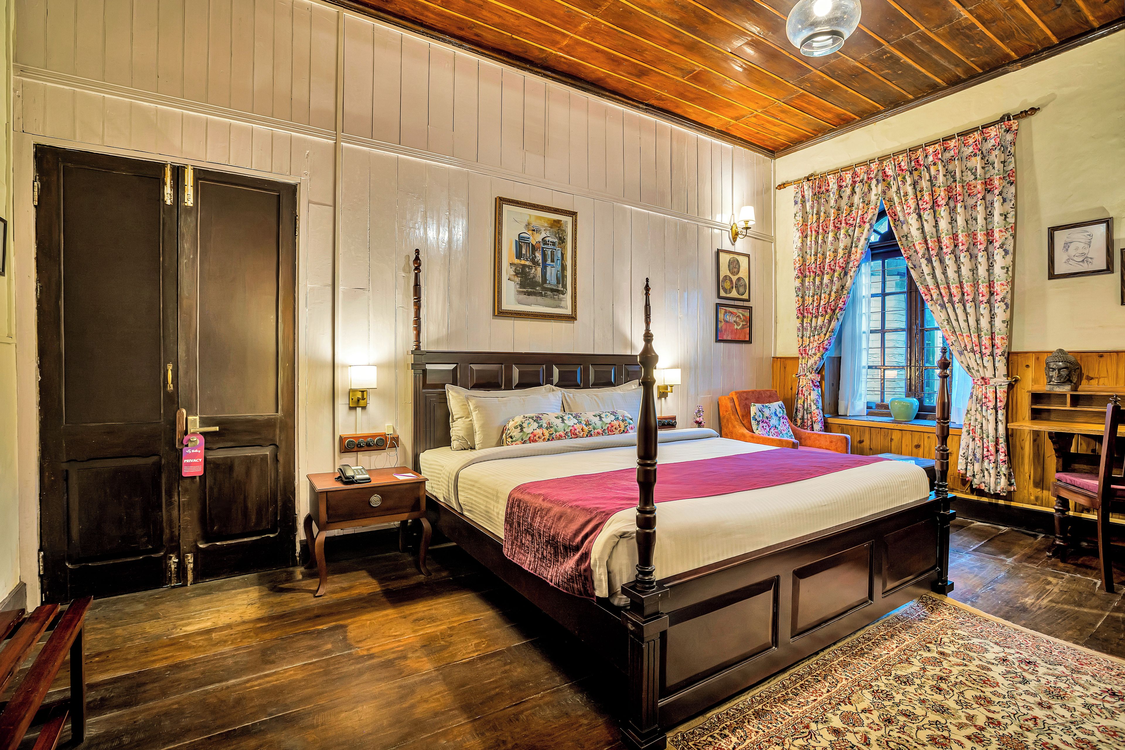 Habitación tradicional con cama con dosel, suelo de madera y un amplio ventanal con cortinas florales.
