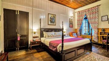 Habitación tradicional con cama con dosel, suelo de madera y un amplio ventanal con cortinas florales.