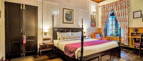 A traditional room with a four-poster bed, wooden flooring, and a large window with floral curtains.