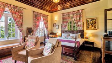 A room with a bed, two armchairs, a wooden ceiling, and a painting on the wall.
