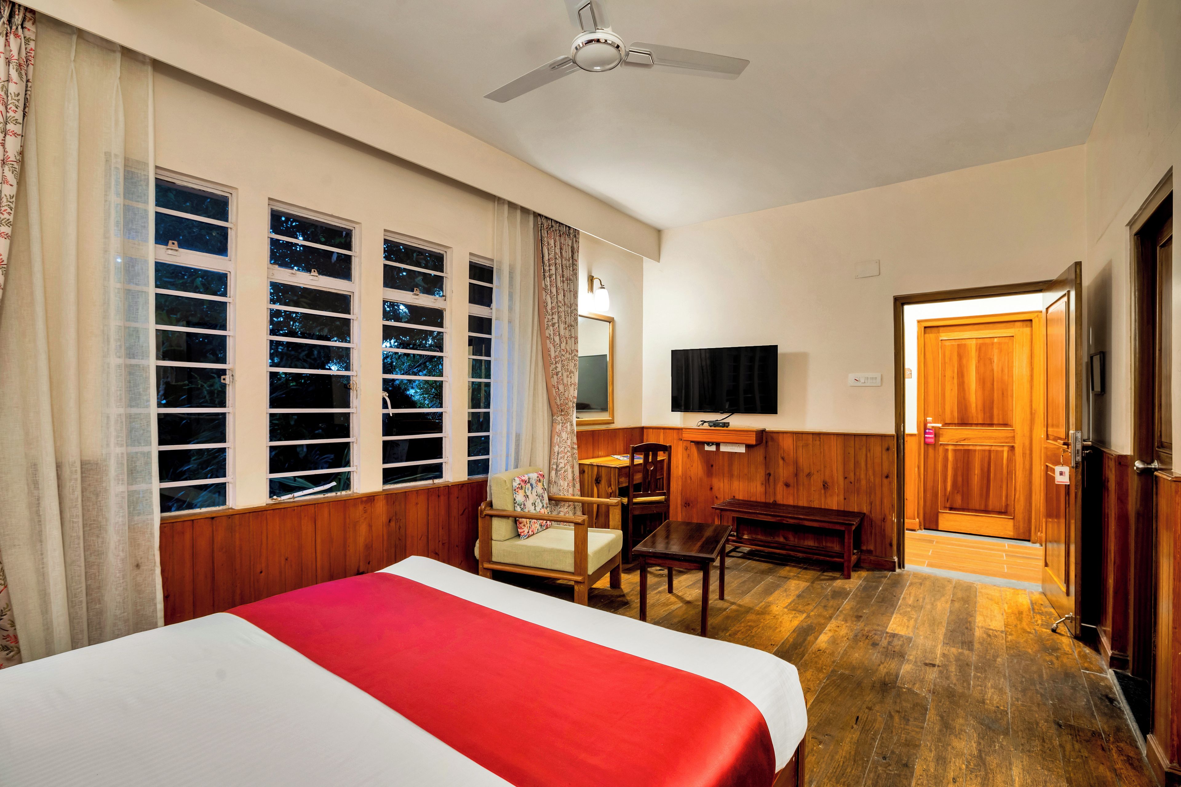 A hotel room with a bed, a desk, a chair, a television, and a door.