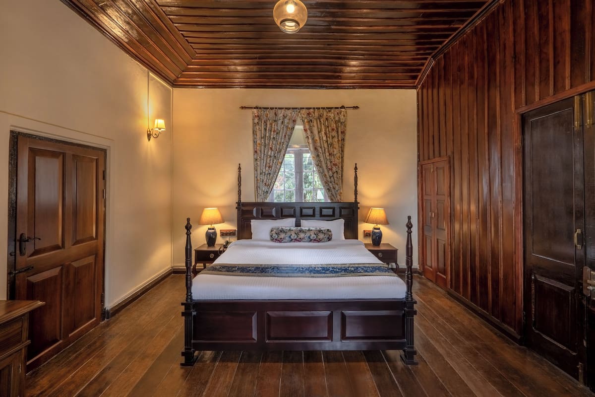 A large wooden bed with a headboard, flanked by nightstands with lamps, in a room with wooden paneling and a ceiling light fixture.