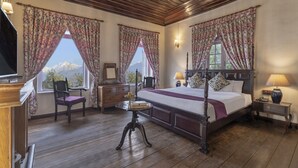 A bedroom with a four-poster bed, wooden flooring, floral curtains, and a view of mountains through the windows. - Sterling Park Kalimpong (Kalimpong)
