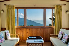 A room with a wooden paneled wall, a window with curtains, a sofa, a chair, and a table with a magazine. - Sterling Park Kalimpong (Kalimpong)