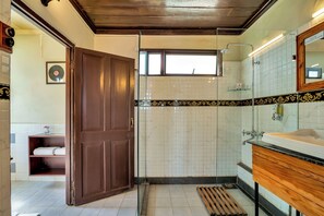 A bathroom with a wooden door, a shower area, a vanity with a mirror, and a shelf with towels. - Sterling Park Kalimpong (Kalimpong)